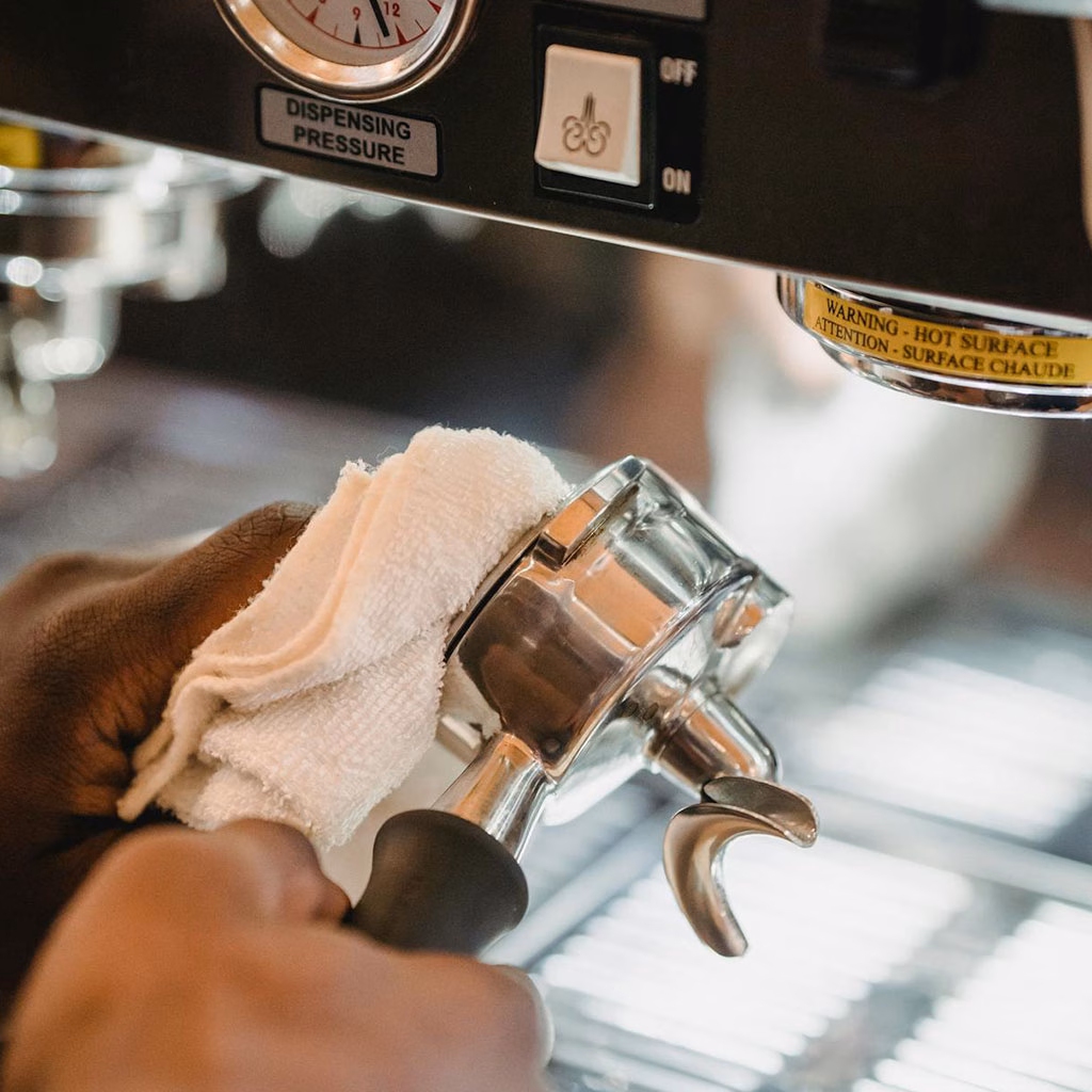 zwei Hände reinigen einen Siebträgereinsatz